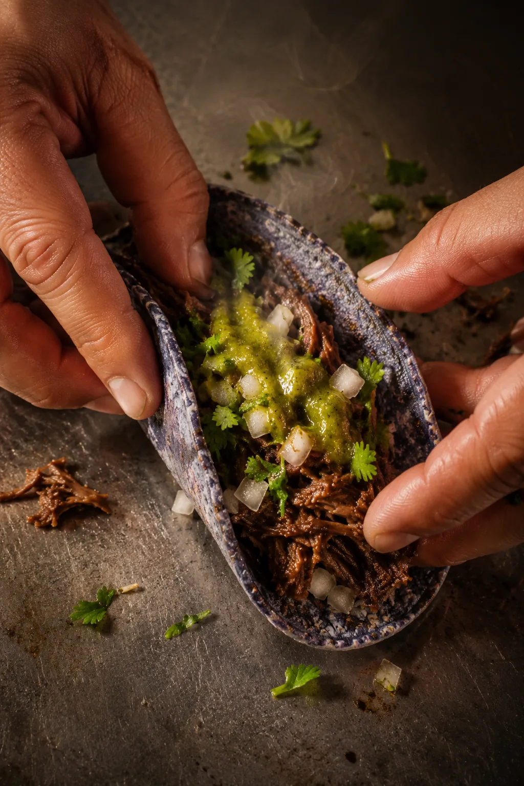 A taco being assembled by hand with barbacoa, onion and cilantro.